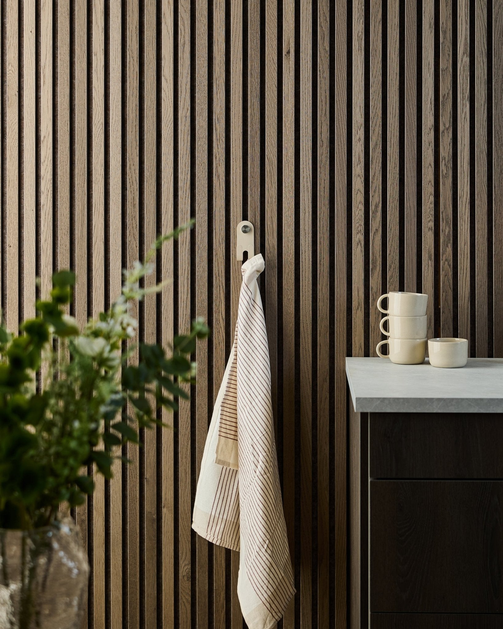 Norr single hanger in beige on Akupanel acoustic slat wall with striped towel and stacked mugs on counter